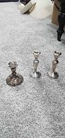 Three weighted sterling candlesticks on carpet