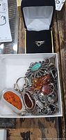 Overview of jewellery lot in boxes showing pendants with amber and green stones, earrings, and ring box
