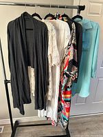 Rack showing five visible garments: grey lace-trim cardigan, cream crochet cardigan, white lace cover-up, multicolour kimono cover-up, teal shirt cover-up
