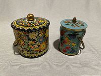 Both tins side by side showing relative size, patterns, lids, handles
