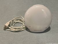 Front view of white spherical Westclox sunrise alarm clock with cord