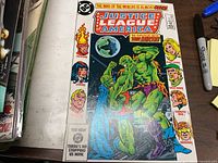 Front cover of Justice League of America #230 comic book on tabletop, partial stack of other comics at left