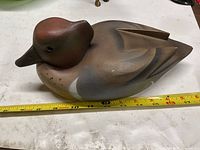Left side view of painted wooden duck decoy with measuring tape indicating length
