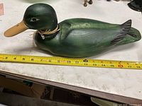 Left side profile of green wooden duck decoy beside ruler showing length
