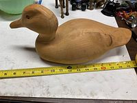 Left side view of carved wooden duck decoy with tape measure showing length