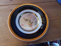 Front of plate showing black and gold rim and central bird chokin design