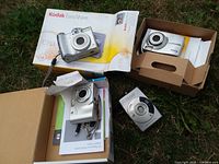 Overview of four digital cameras with packaging and manuals