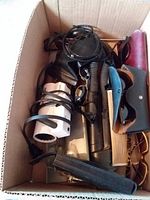 Top view of box showing mixed sunglasses, cases, flashlight, cylindrical electronic device and cords
