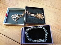 Gold-tone necklace with charm and silver-tone braided bracelet shown in open boxes on wooden surface
