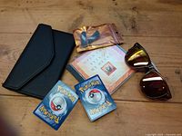 All items: wallet, sunglasses, book, earbuds in bag, two Pokémon cards