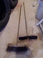 Two push brooms lying on floor, showing full handles and bristle heads