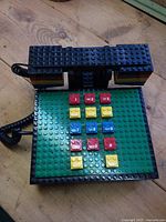 Top view of Lego telephone base showing green baseplate, multicoloured keypad, handset on cradle