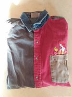 Folded color-block shirt showing denim collar, buttons, pocket, embroidery