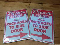 Pair of identical red, white and blue metal delivery signs on wood surface