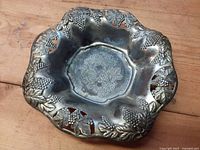 Top view showing scalloped pewter bowl, pierced grape and leaf rim, embossed fruit design in centre