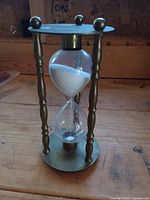 Full view of brass and glass hourglass standing on wood surface