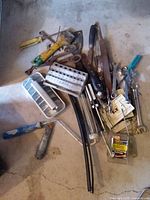 Pile of assorted hand tools, ice cube tray, hoses, and hardware on floor