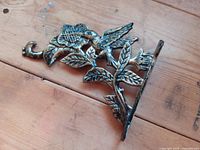 Full view of brass hook lying flat showing hummingbird and floral design