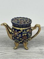 Front view of gold and navy blue teapot-shaped trinket box on three legs