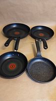 Four frying pans displayed: three T-fal, one The Rock