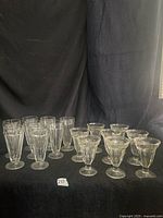Group of sixteen clear pressed glass parfait and sundae dishes arranged on dark backdrop