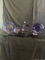Front view showing stacks and samples of cobalt blue glass plates, smaller plates, bowls, and plastic chargers