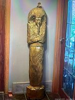 Full view of gold/bronze Egyptian pharaoh floor statue standing against wall