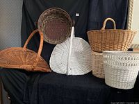 Group shot of six assorted wicker baskets in natural tan, brown and white finishes arranged on black backdrop