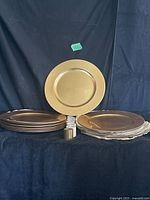 Stack of gold-tone charger plates with one plate displayed upright; napkin rings visible in front
