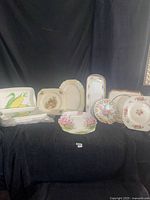 Whole lot of 11 decorative ceramic serving trays and plates arranged on black cloth