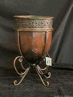 Front view of hammered copper-tone planter on scrolled wrought iron stand showing overall form and patina