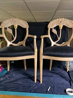 Front view of both carved-back armchairs showing floral fan motif, gilt accents, black upholstered seats