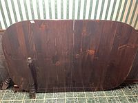 Two dark walnut-stained tabletop halves with rounded corners leaning against wall; turned legs visible at side