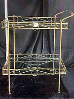Front view of gold-tone two-tier cart frame showing scroll design, handle, single glass bottom shelf and missing top glass