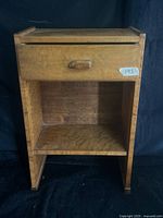 Full view of nightstand showing drawer, open shelf, wood tone, wear marks and sticker residue