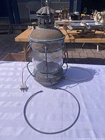 Front view of copper nautical lantern with cord and plug; suspension ring laid in front