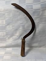 Full view of curved iron sickle with wooden handle