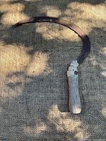 Full view of sickle on burlap showing curved blade and handle