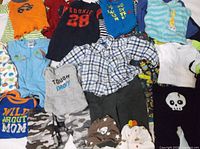 Overall view of assorted baby clothing items laid out including shirts, pants, rompers, hats