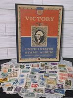 Front cover of Victory United States Stamp Album standing behind assortment of loose U.S. stamps