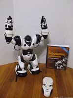 Robot with raised arms, remote, and book visible