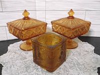 Group view of two lidded pedestal candy dishes and one square dish