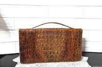 Front view of brown alligator skin clutch with top handle