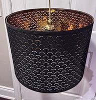 Full view of pendant light showing black perforated shade and gold interior
