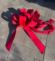 Full view of large red bow on pavement showing loops and tails