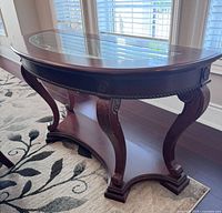 Three-quarter view of demilune table showing glass top and carved legs