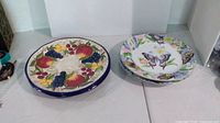 Two fruit design plates and stack of butterfly design plates displayed on table