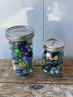 Two mason jars filled with assorted marbles on wood surface