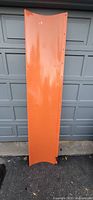 Full view of orange SnowBear plow blade leaning on garage door