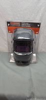 Front view of grey Shop Iron welding helmet in packaging